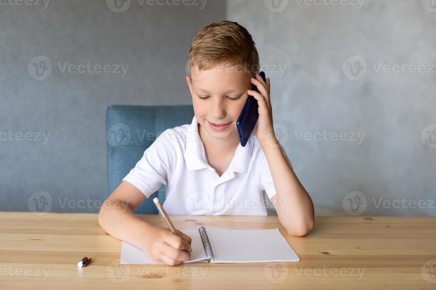 Cute boy writes in an open notebook and looks at the phone. photo