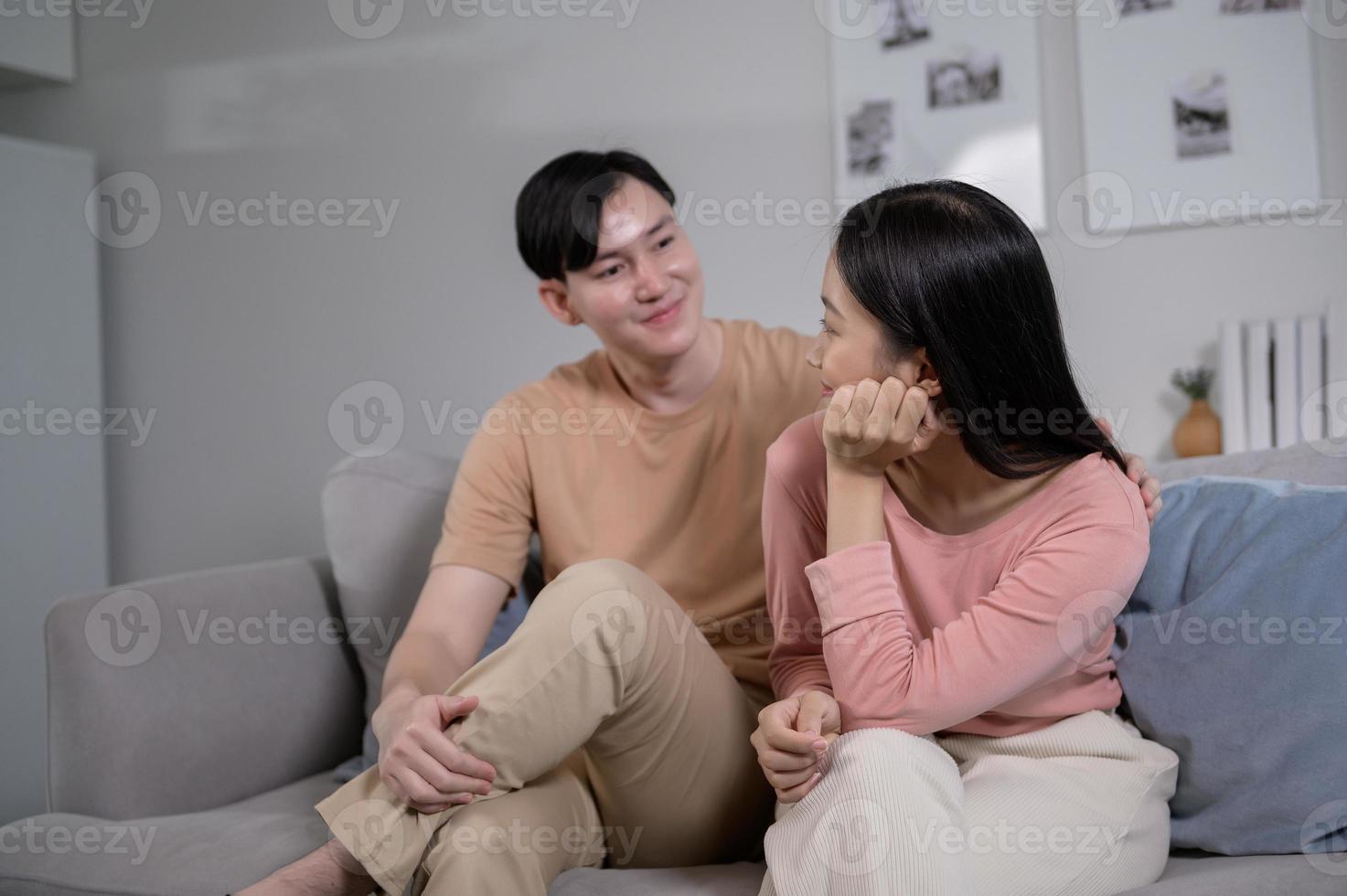 Happy young Asian couple sitting on sofa relaxing together in living room at home photo