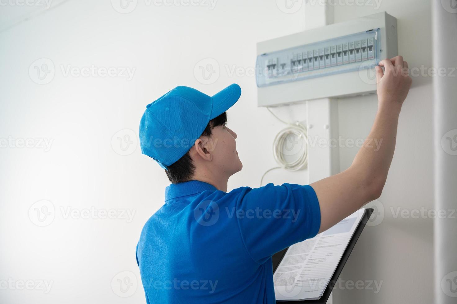 un asiático joven técnico Servicio hombre vistiendo azul uniforme comprobación eléctrico accesorios en hogar foto