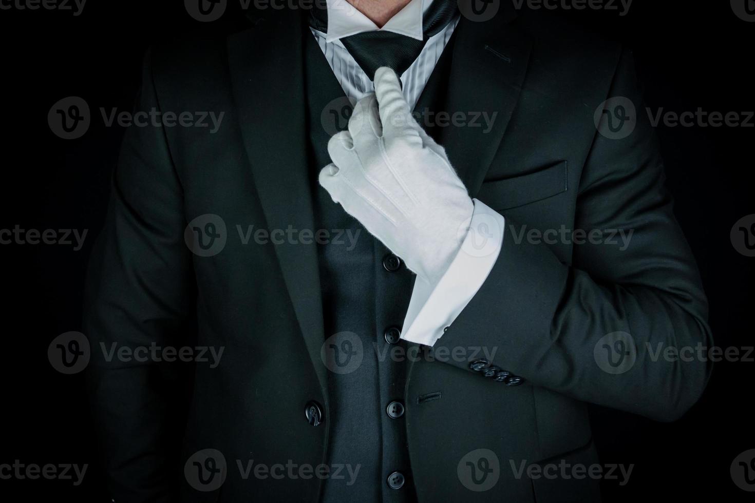 Isolated Close-Up of Butler or Concierge in Dark Suit and White Gloves Straightening Tie. Service Industry and Professional Hospitality. photo
