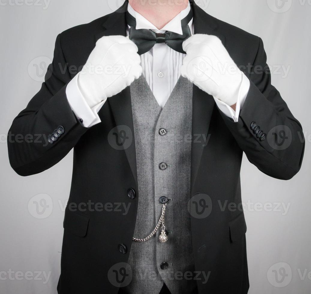 Portrait of Butler in Dark Formal Suit and White Gloves Straightening Bow Tie. Service Industry and Professional Hospitality. photo