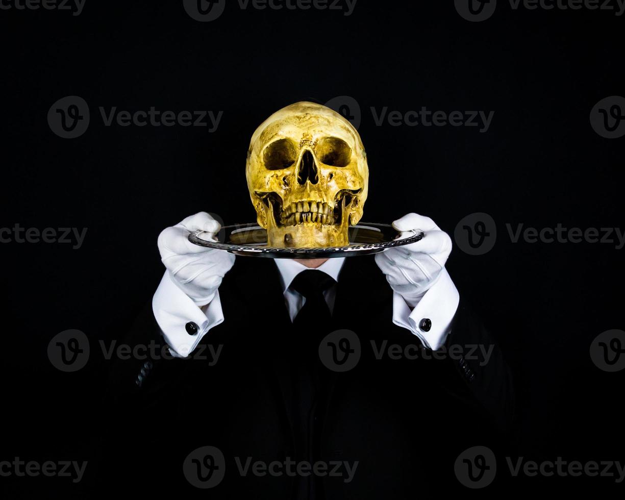 Portrait of Butler or Waiter in Dark Suit and White Gloves Holding Skull on Tray. Concept of Horror and Halloween.  Disturbing and Frightful Death. photo