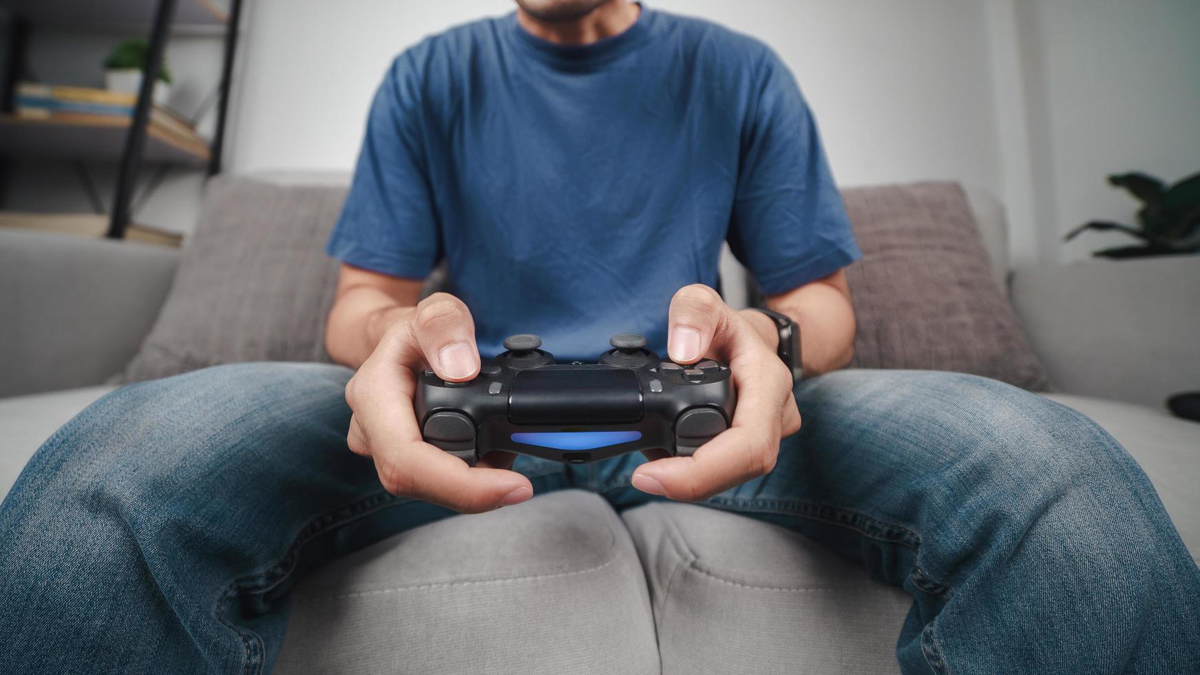 Excited young handsome man holding joystick controller playing video game sitting on the couch at home photo