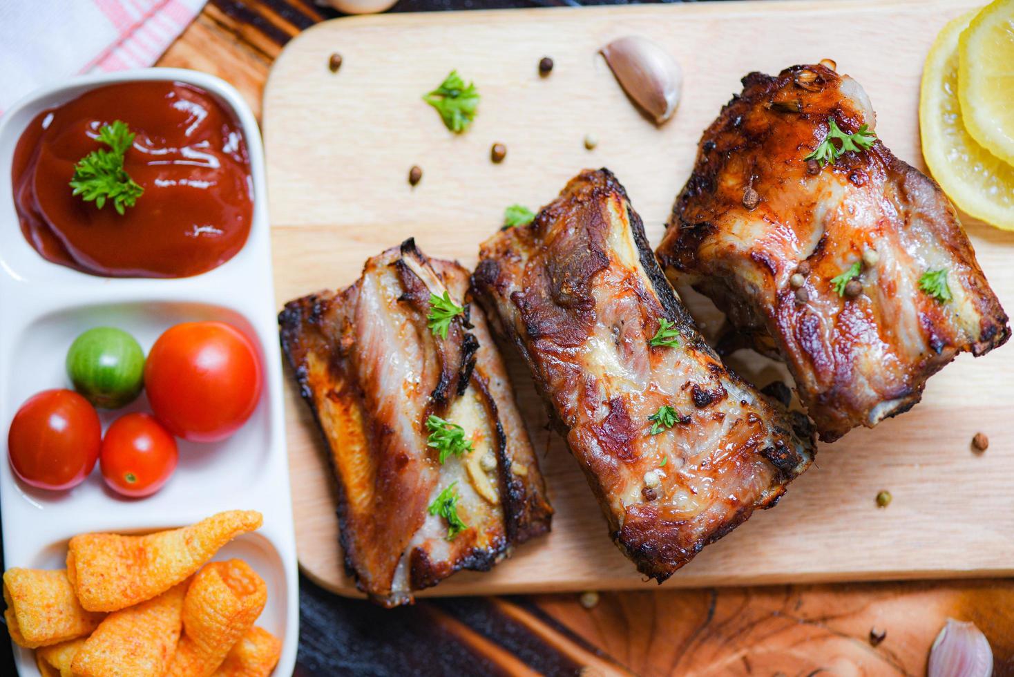bbq pork ribs grilled with tomatoes ketchup and herbs spices served on the wooden cutting board on table - Roasted barbecue pork spare rib sliced photo