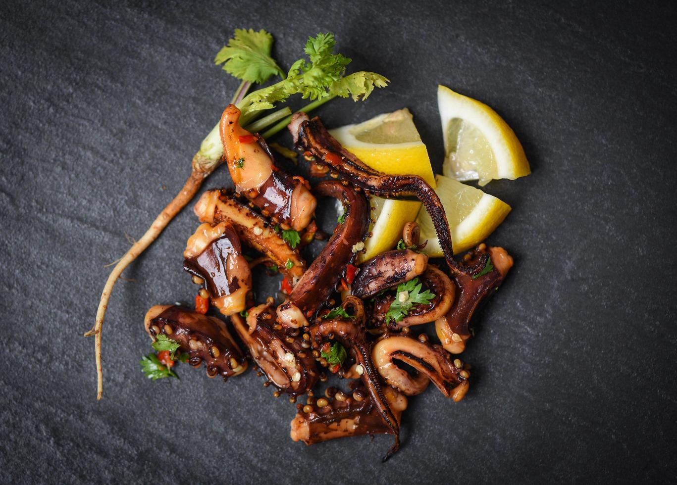 octopus salad with lemon herbs and spices on dark background top view - Tentacles squid grilled appetizer food hot and spicy chilli sauce seafood cooked served on black plate in the restaurant photo