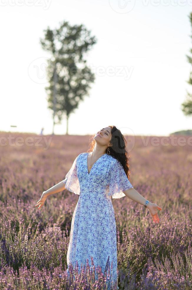 retrato de un contento mujer en un azul vestir disfrutando un soleado verano día en un lavanda campo. Fresco aire, estilo de vida. foto