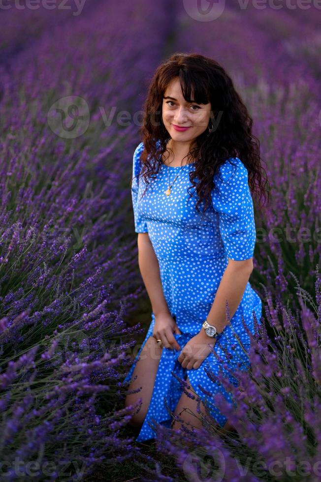 retrato de un contento mujer en un azul vestir disfrutando un soleado verano día en un lavanda campo. Fresco aire, estilo de vida. foto