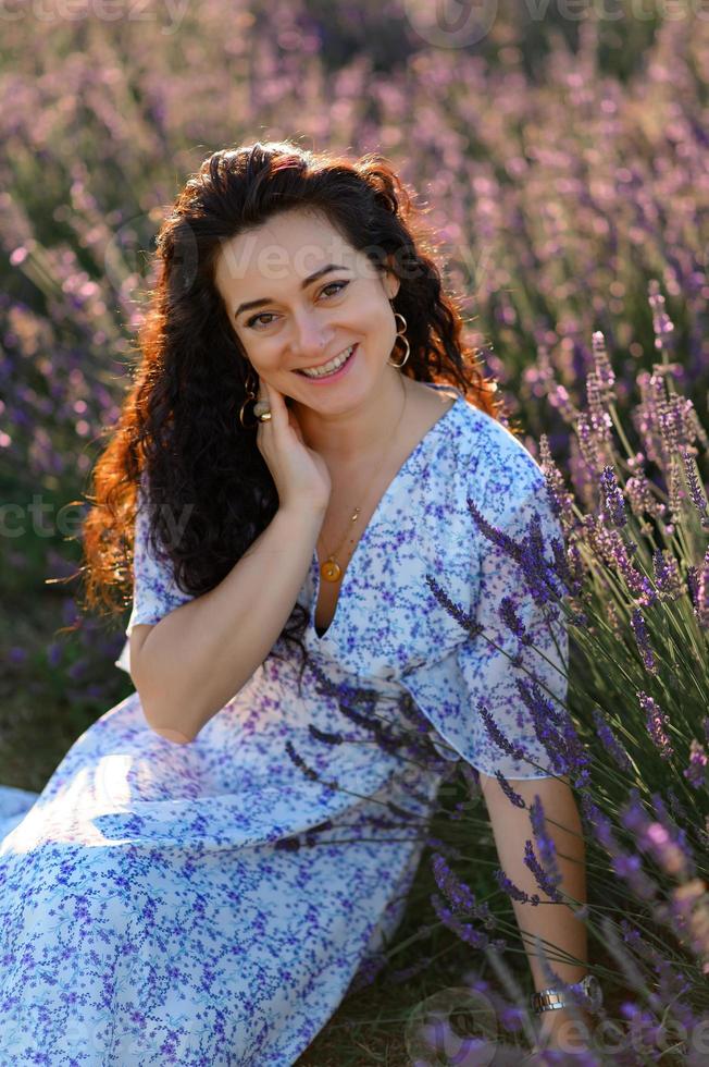 retrato de un contento mujer en un azul vestir disfrutando un soleado verano día en un lavanda campo. Fresco aire, estilo de vida. foto