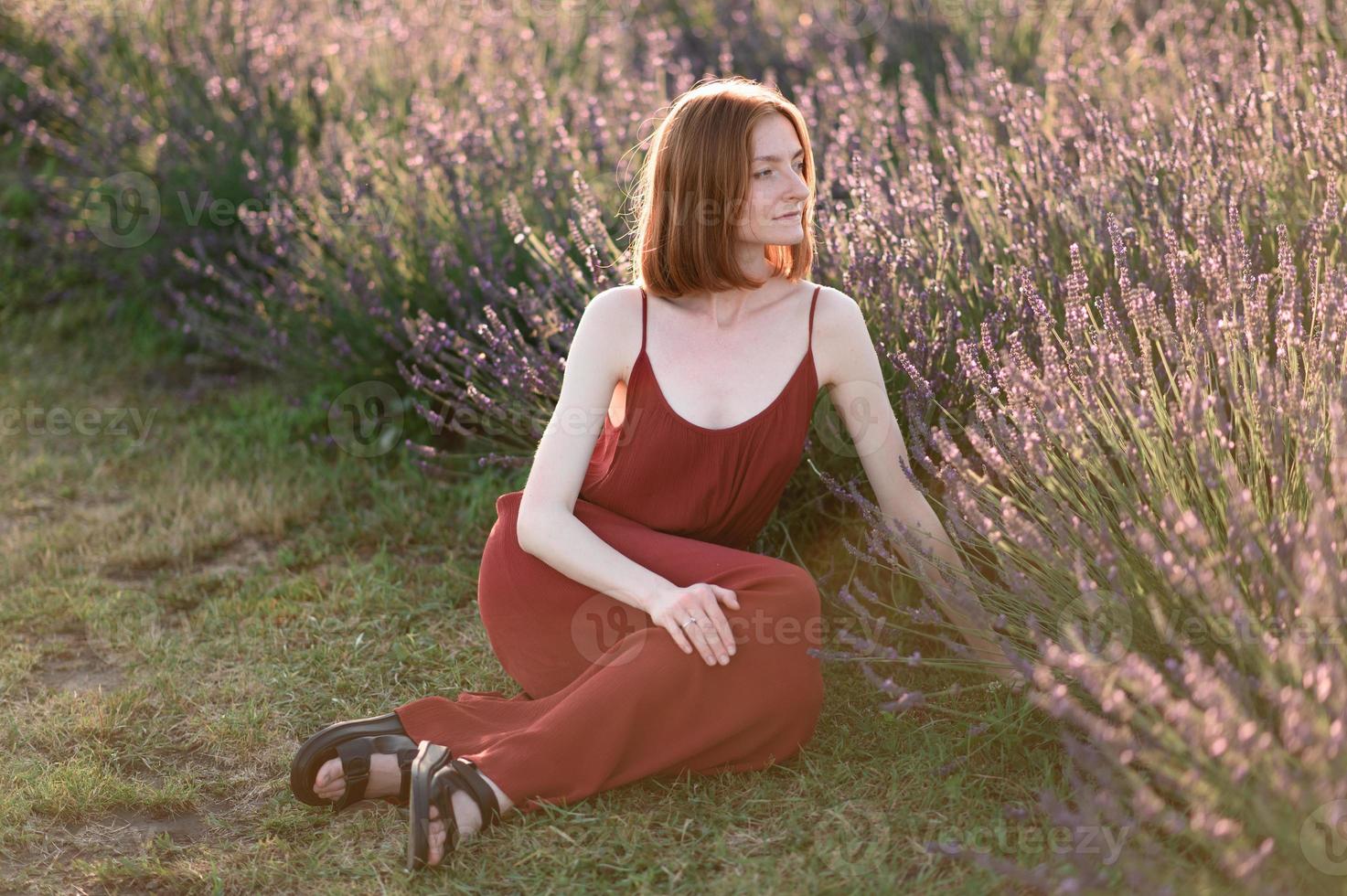 A red-haired young girl without make-up is resting in a lavender field. Summer vacation and travel time. photo