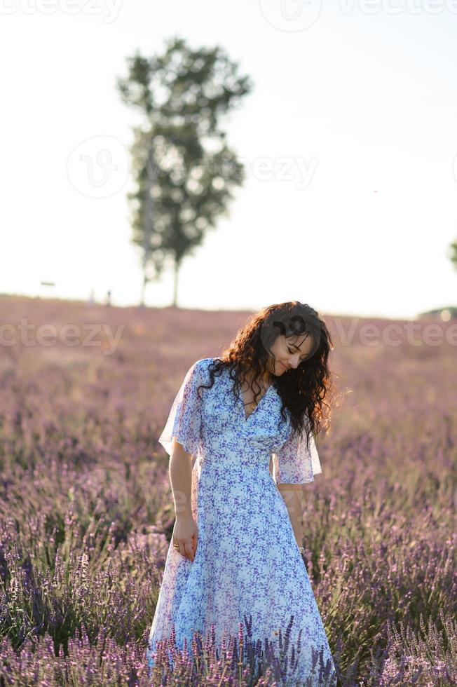 retrato de un contento mujer en un azul vestir disfrutando un soleado verano día en un lavanda campo. Fresco aire, estilo de vida. foto