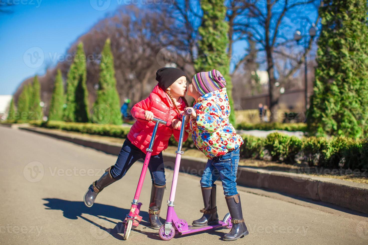 Little sisters riding scooters outdoors photo