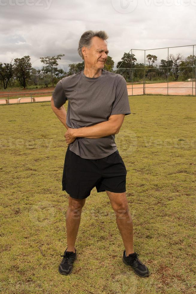 Mature man outside on the grass doing Stretches before working out photo