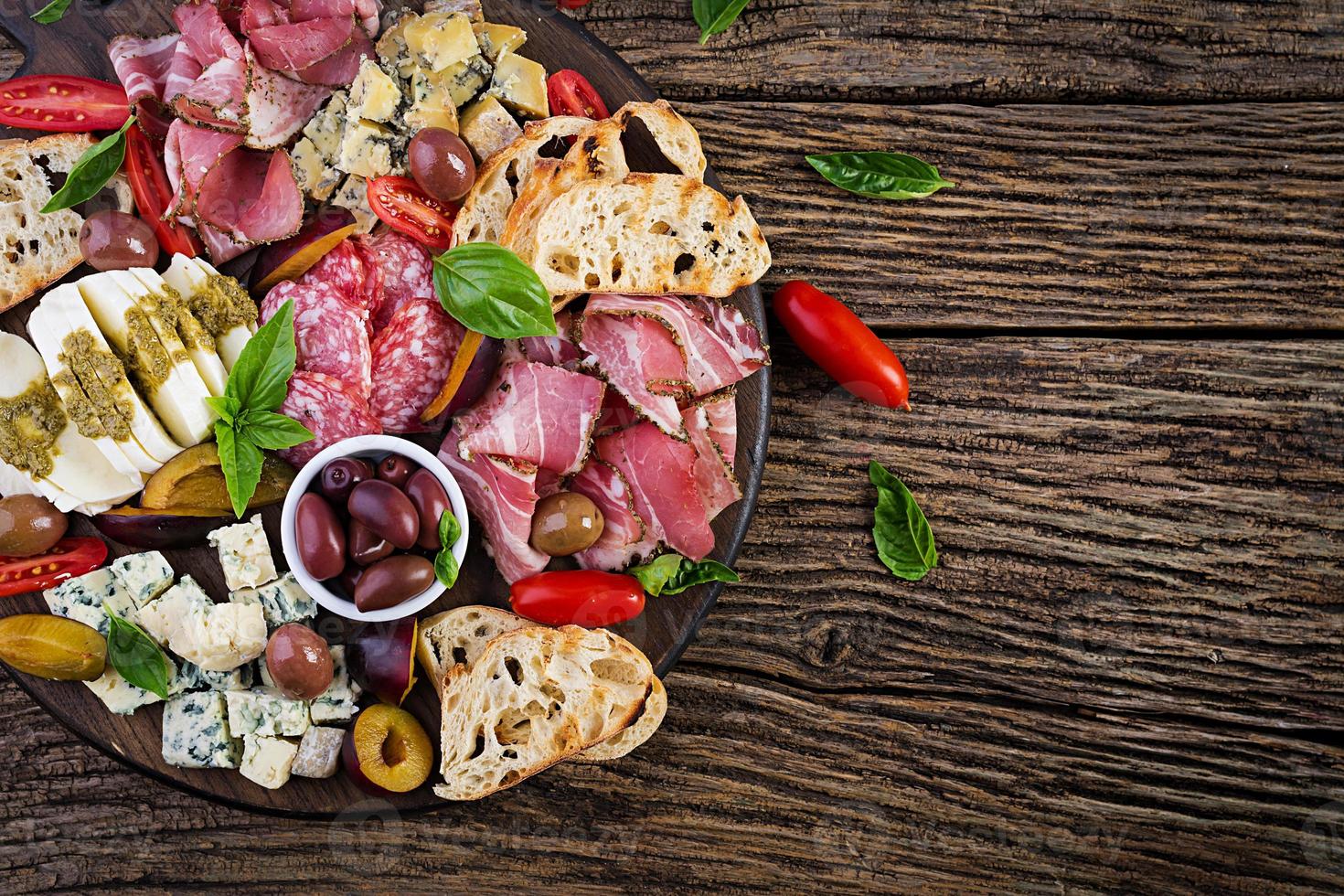 Antipasto platter with ham, prosciutto, salami, blue cheese, mozzarella with pesto and olives on a wooden background. Top view, overhead photo