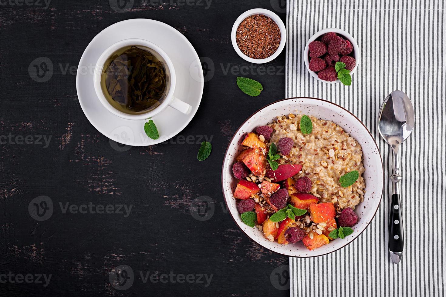 Oatmeal porridge with raspberry and peach on dark background. Healthy breakfast. Vegetarian food. Top view photo