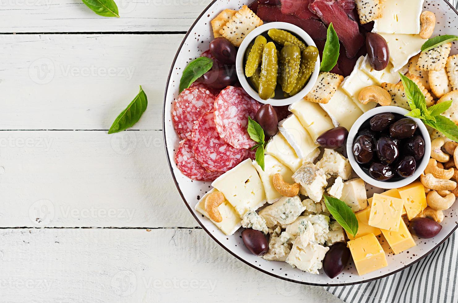 Antipasto platter with basturma, salami, blue cheese, nuts, pickles and olives on a white wooden background. Top view, overhead photo