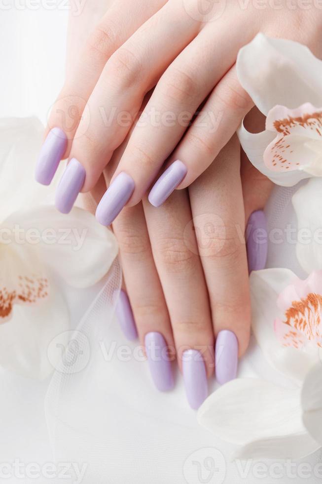 manos de niña con delicada manicura púrpura y flores de orquídeas foto