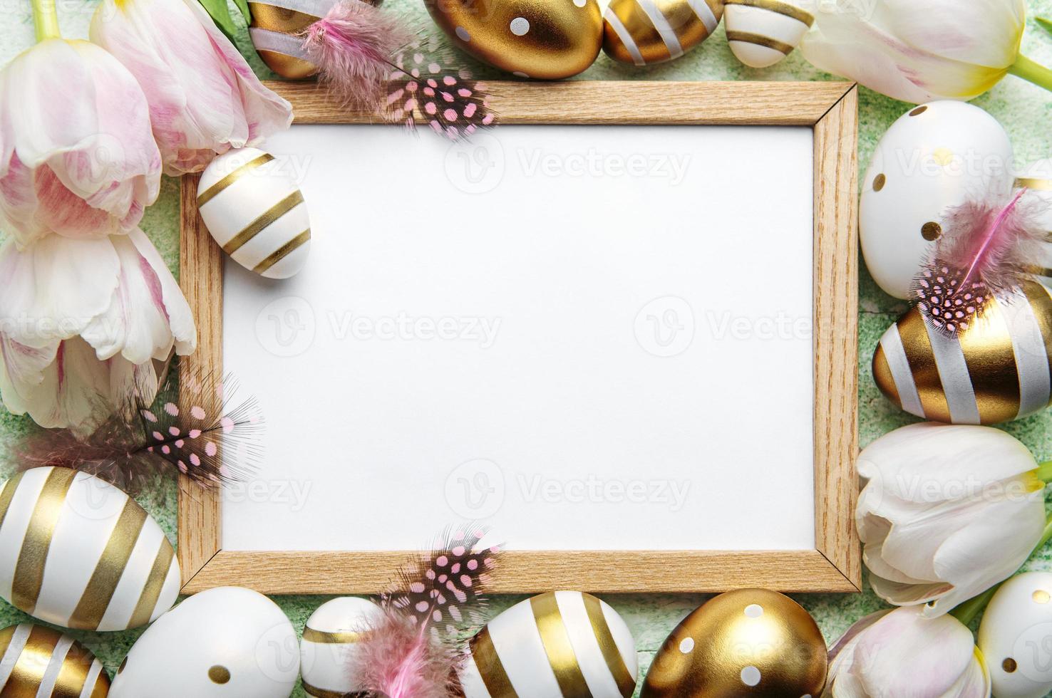 Blank picture frame surrounded by Easter eggs and tulip flowers on green background photo