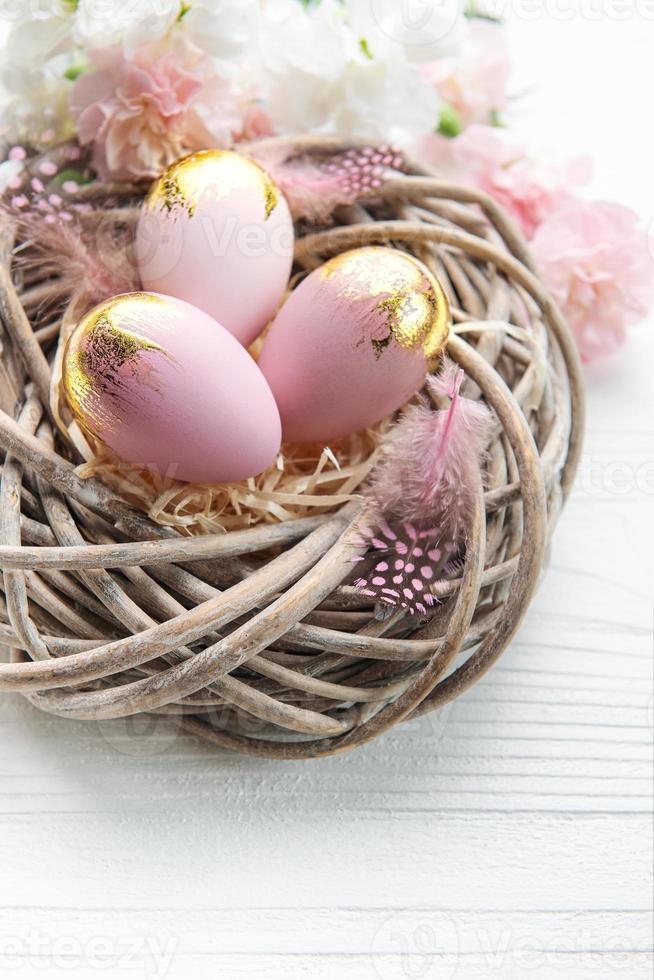 Easter eggs painted pink and gold and  feathers in a nest on a white wooden background. photo
