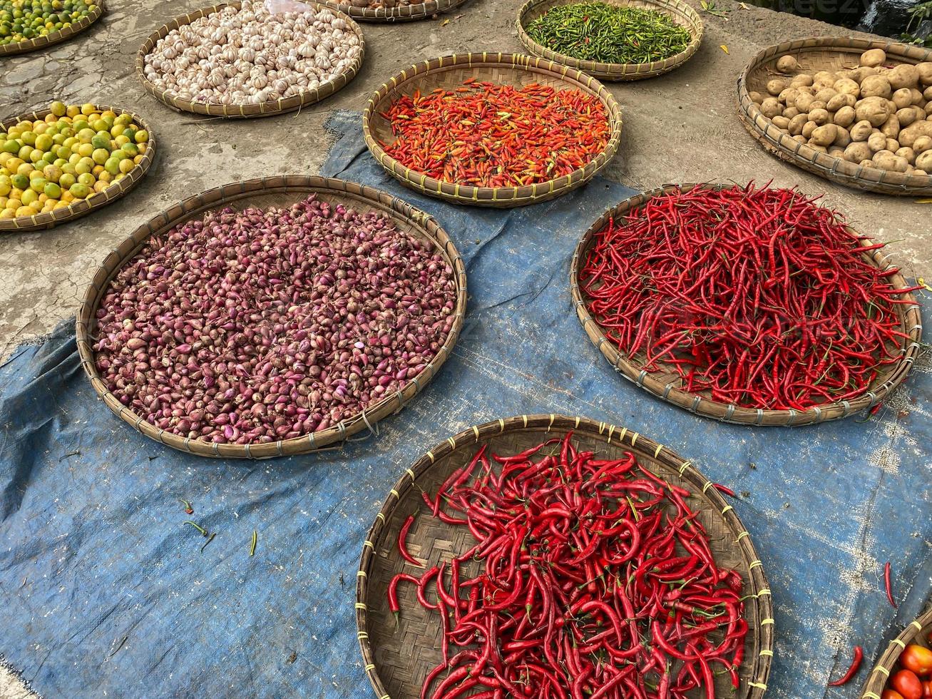 various vegetables tomatoes, chilli, red onion, corn, carrot, lime, garlic being sold at asian traditional market. colorful vegetables on round bamboo tray at traditional market floor photo