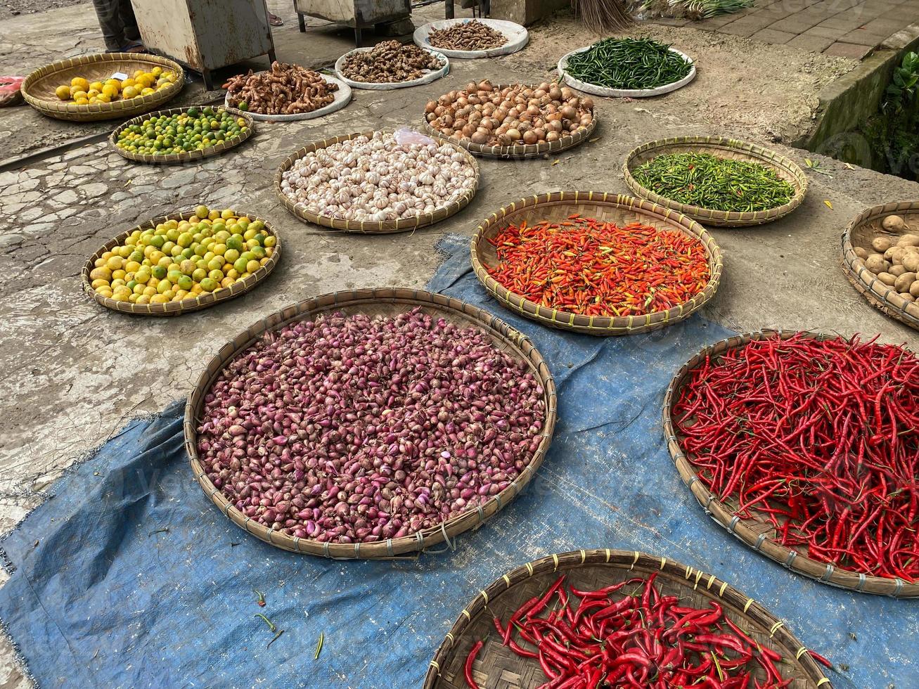 various vegetables tomatoes, chilli, red onion, corn, carrot, lime, garlic being sold at asian traditional market. colorful vegetables on round bamboo tray at traditional market floor photo