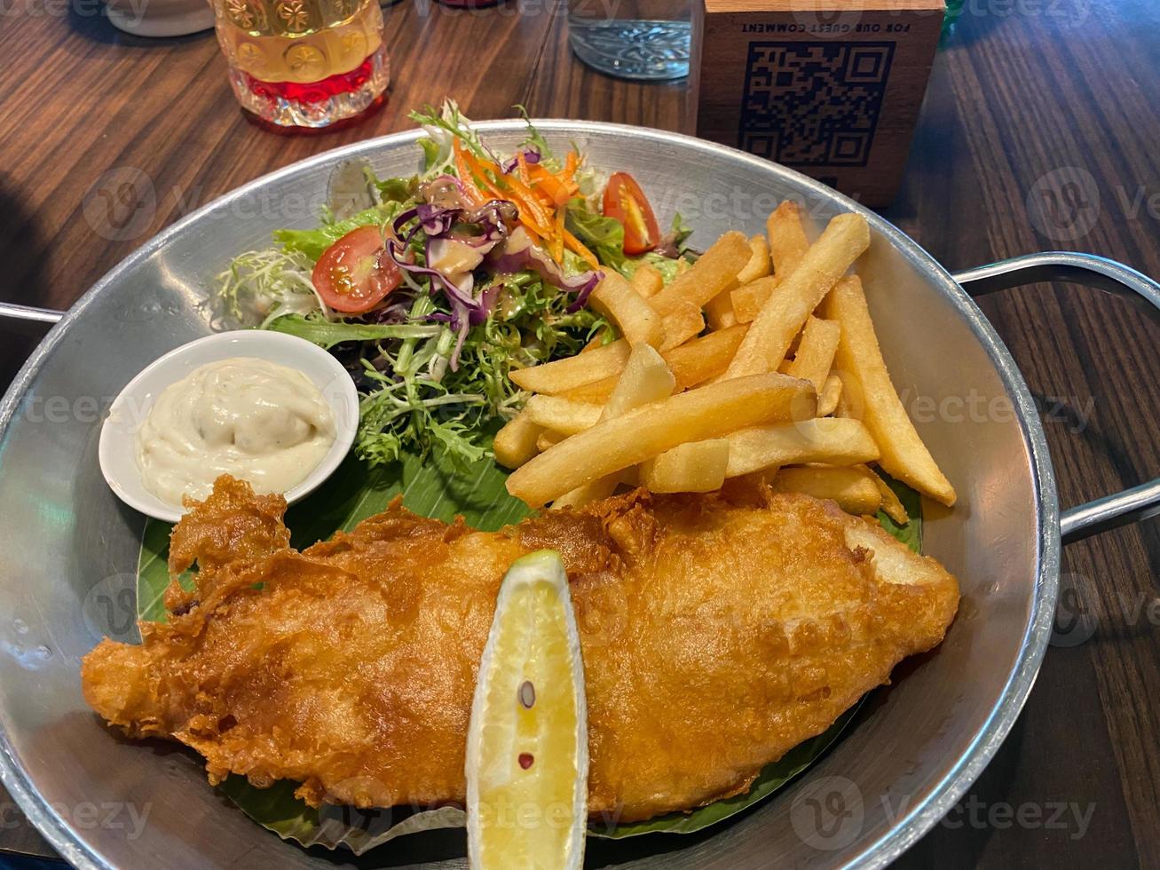 close up view of delicious fish and chips with french fries, caesar salad with balsamic sauce and tartar sauce or mayonnaise photo