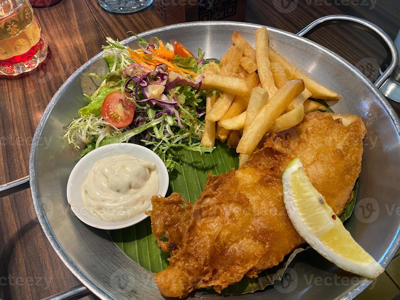 close up view of delicious fish and chips with french fries, caesar salad with balsamic sauce and tartar sauce or mayonnaise photo