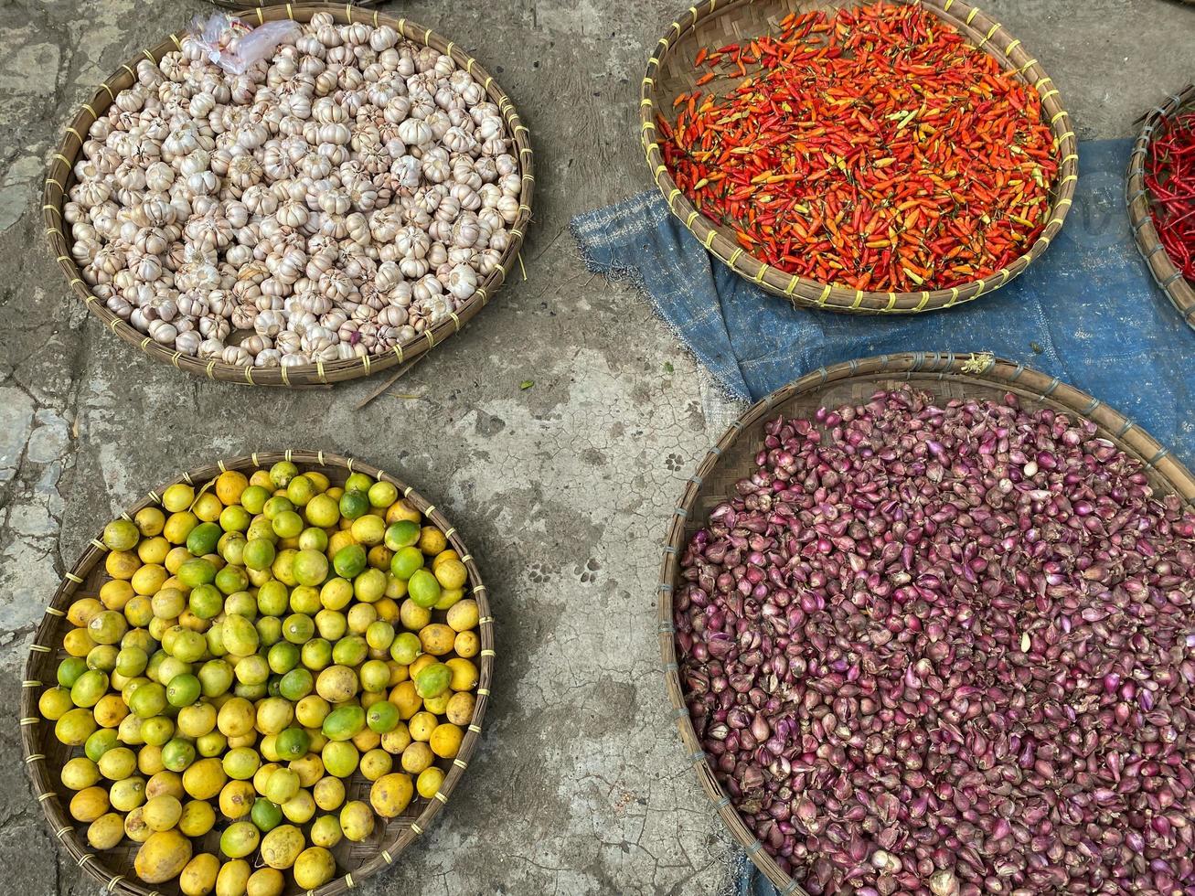 various vegetables tomatoes, chilli, red onion, corn, carrot, lime, garlic being sold at asian traditional market. colorful vegetables on round bamboo tray at traditional market floor photo