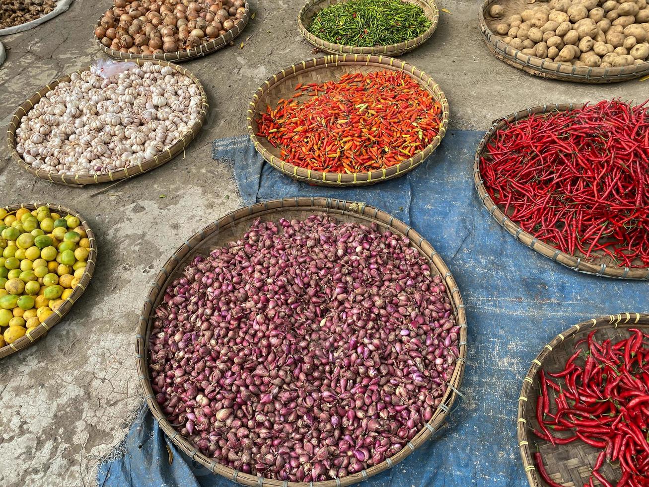 various vegetables tomatoes, chilli, red onion, corn, carrot, lime, garlic being sold at asian traditional market. colorful vegetables on round bamboo tray at traditional market floor photo