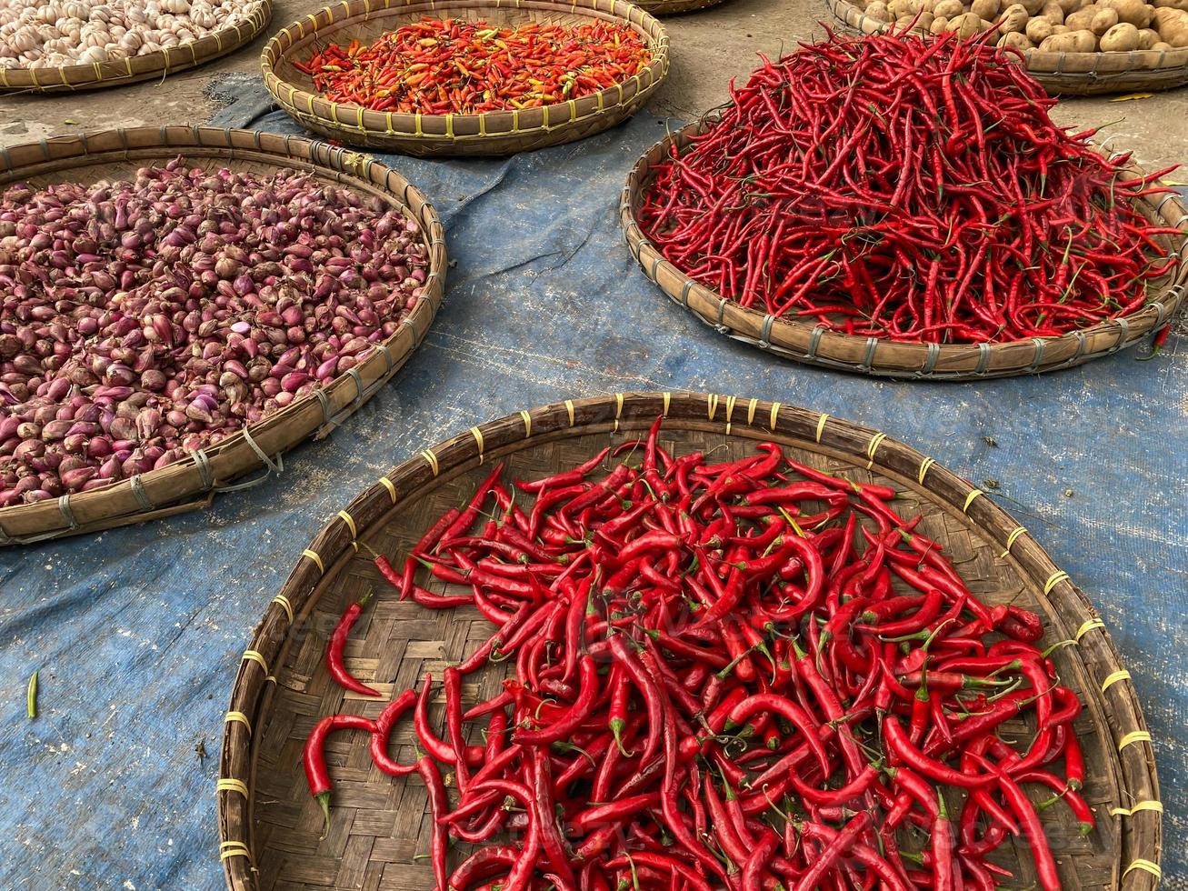 various vegetables tomatoes, chilli, red onion, corn, carrot, lime, garlic being sold at asian traditional market. colorful vegetables on round bamboo tray at traditional market floor photo