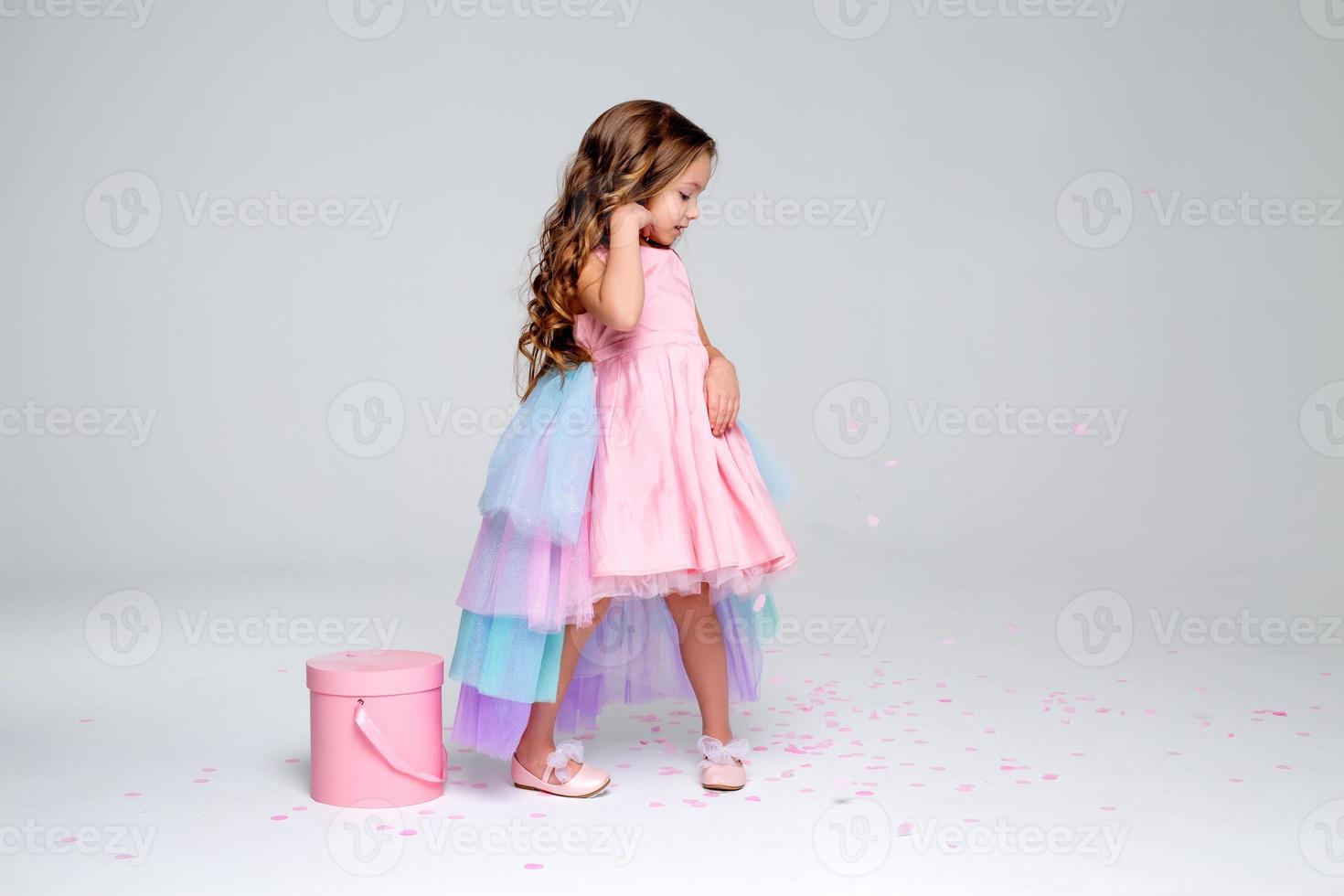 beautiful little girl in a chic pink dress poses sitting on a gray background and throws confetti. fashion and style. space for text. photo in the studio. High quality photo