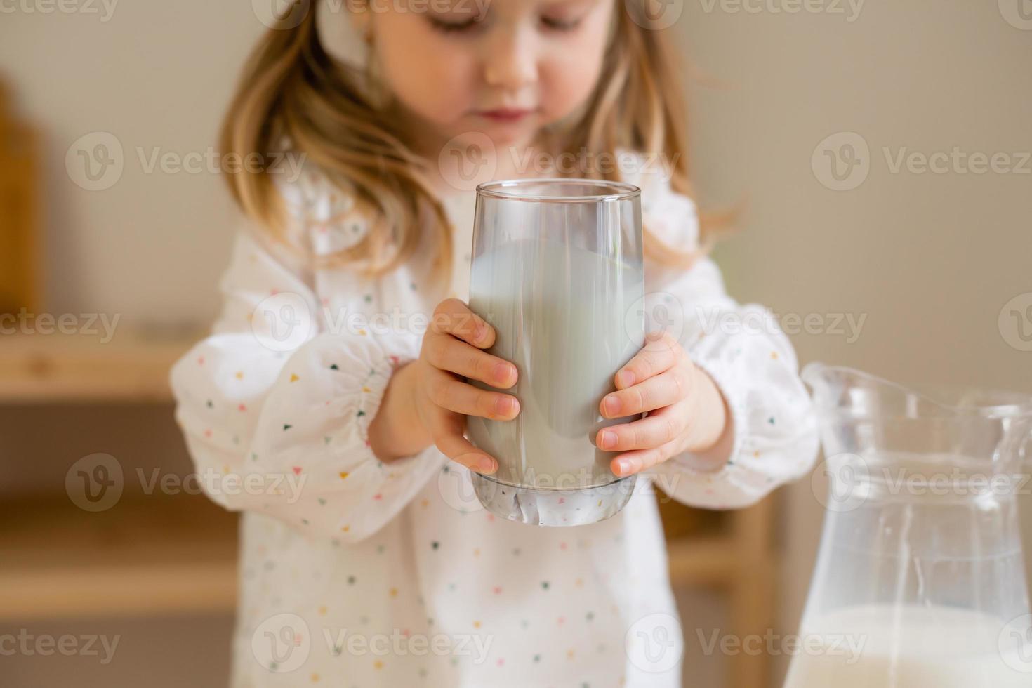 A cute little girl drinks milk at home in a wooden kitchen. Milk Day photo