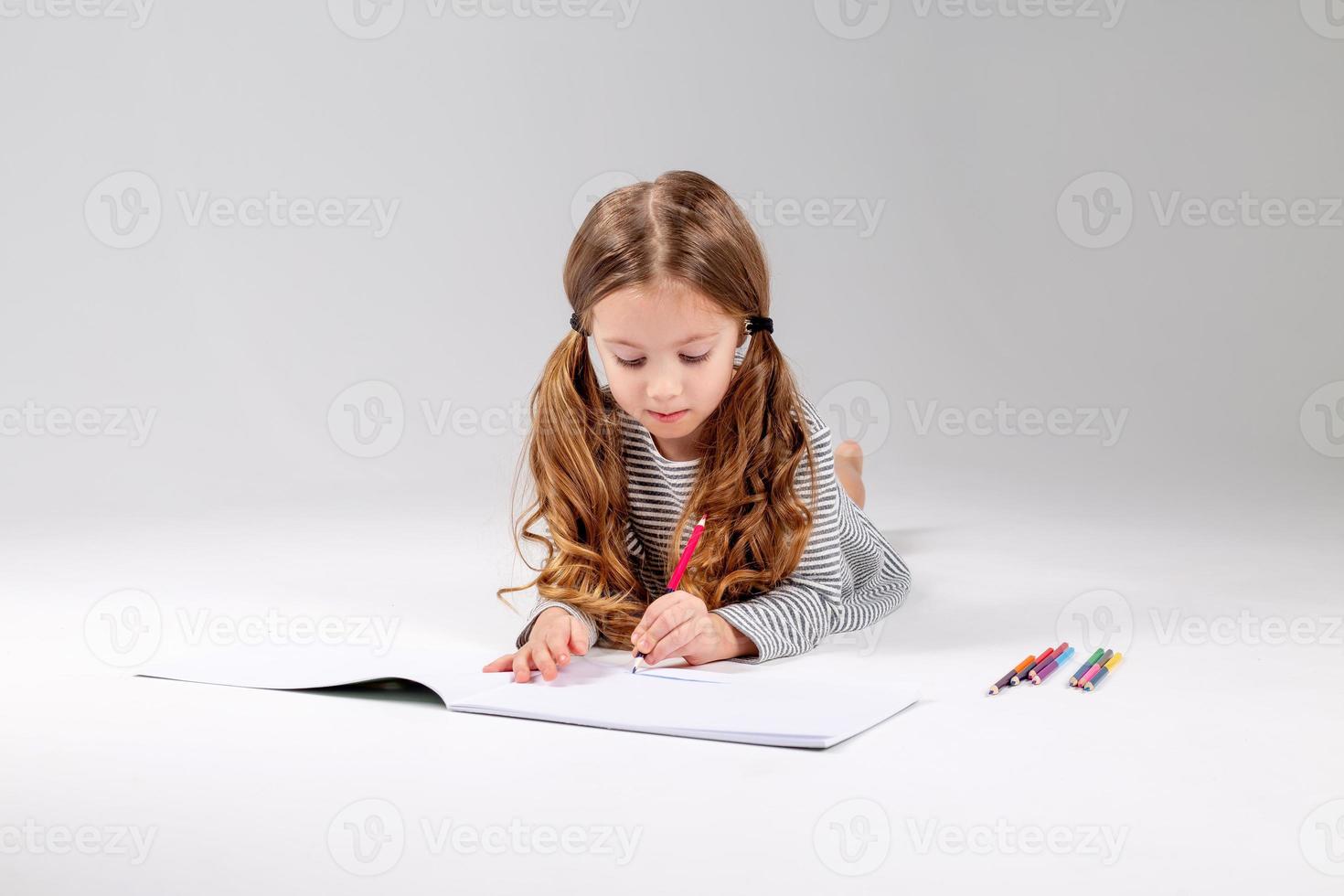 little girl in a striped dress draws in an album lying on the floor. child development. lifestyle. preschool and school education. space for text. High quality photo