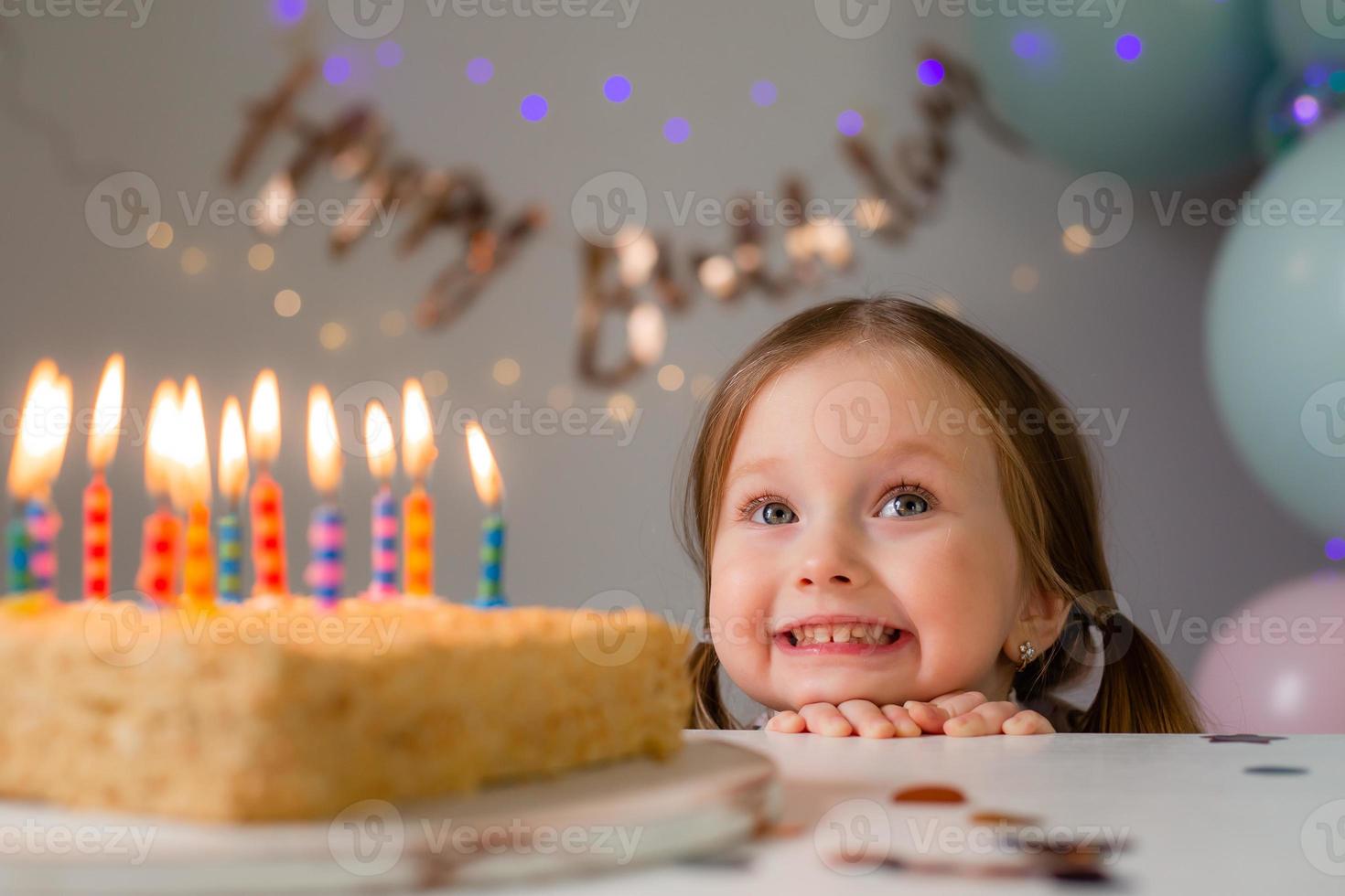 cute little girl blows out candles on a birthday cake at home against a backdrop of balloons. Child's birthday photo