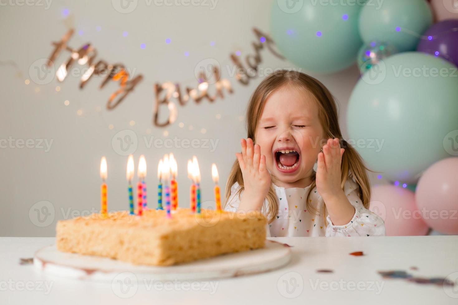 cute little girl blows out candles on a birthday cake at home against a backdrop of balloons. Child's birthday photo