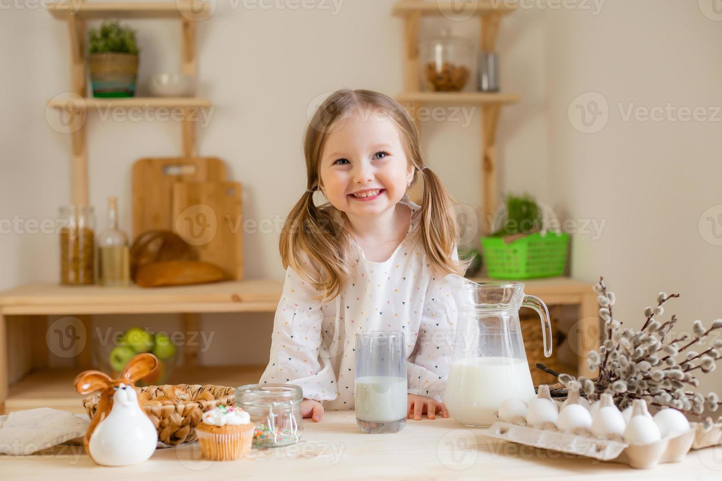 un linda pequeño niña bebidas Leche a hogar en un de madera cocina. Leche día foto