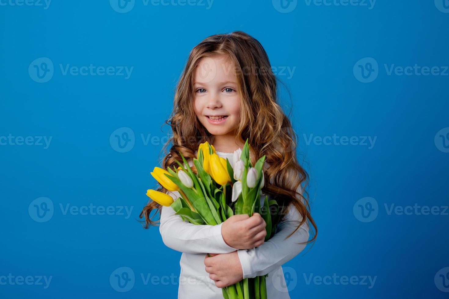 retrato de un encantador sonriente pequeño niña con un ramo de flores de tulipanes en su manos. estilo de vida. Fresco flores internacional De las mujeres día. espacio para texto. alto calidad foto