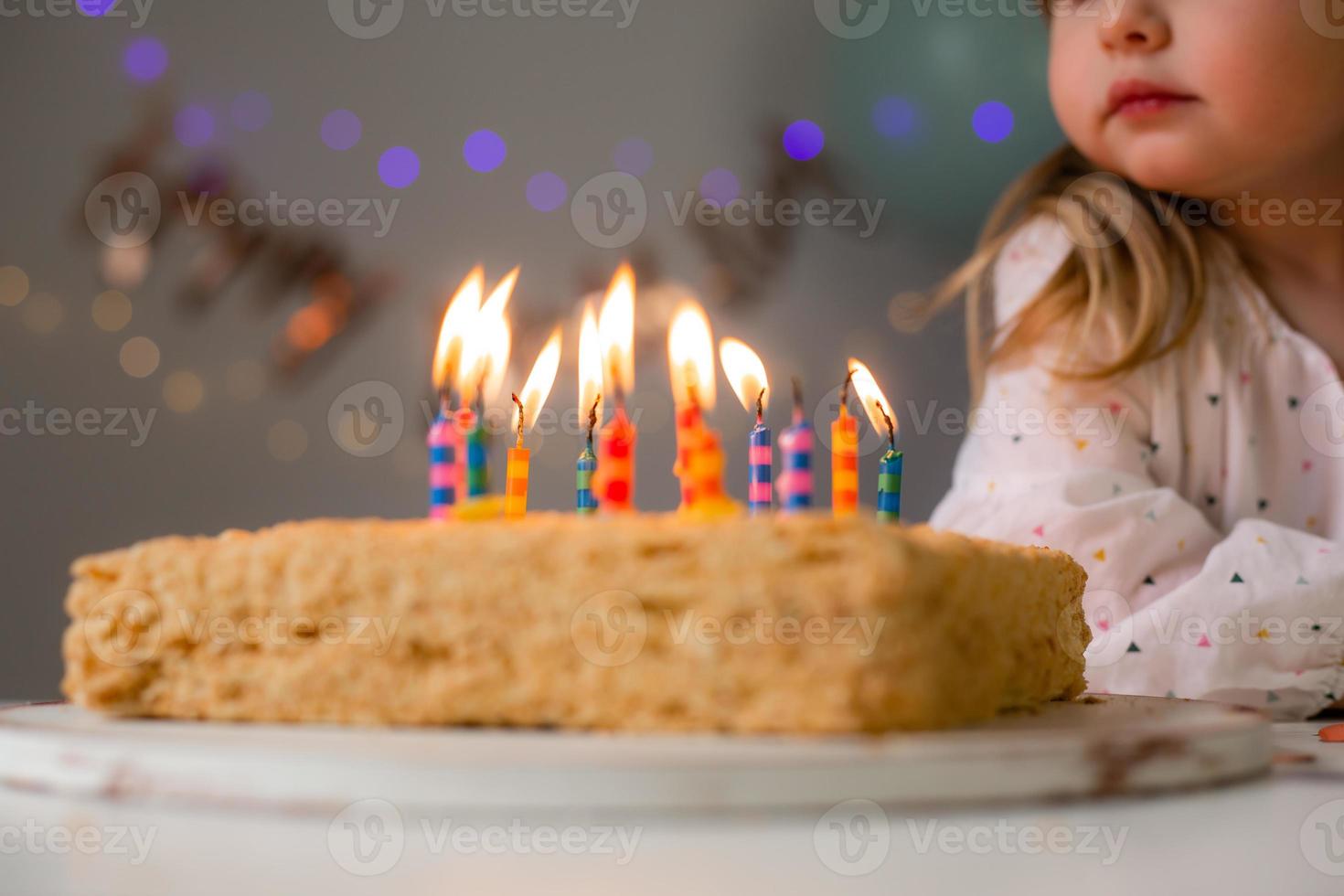 cute little girl blows out candles on a birthday cake at home against a backdrop of balloons. Child's birthday photo