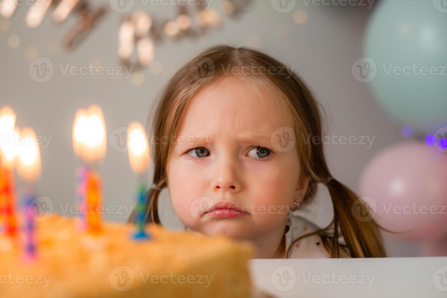 cute little girl blows out candles on a birthday cake at home against a backdrop of balloons. Child's birthday photo