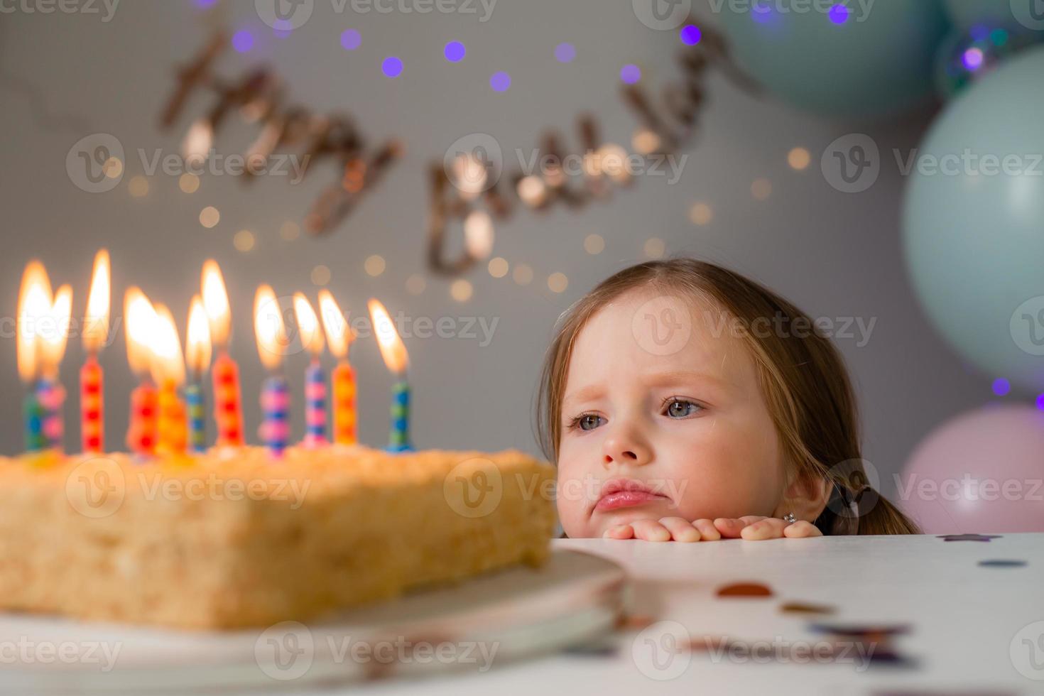 cute little girl blows out candles on a birthday cake at home against a backdrop of balloons. Child's birthday photo