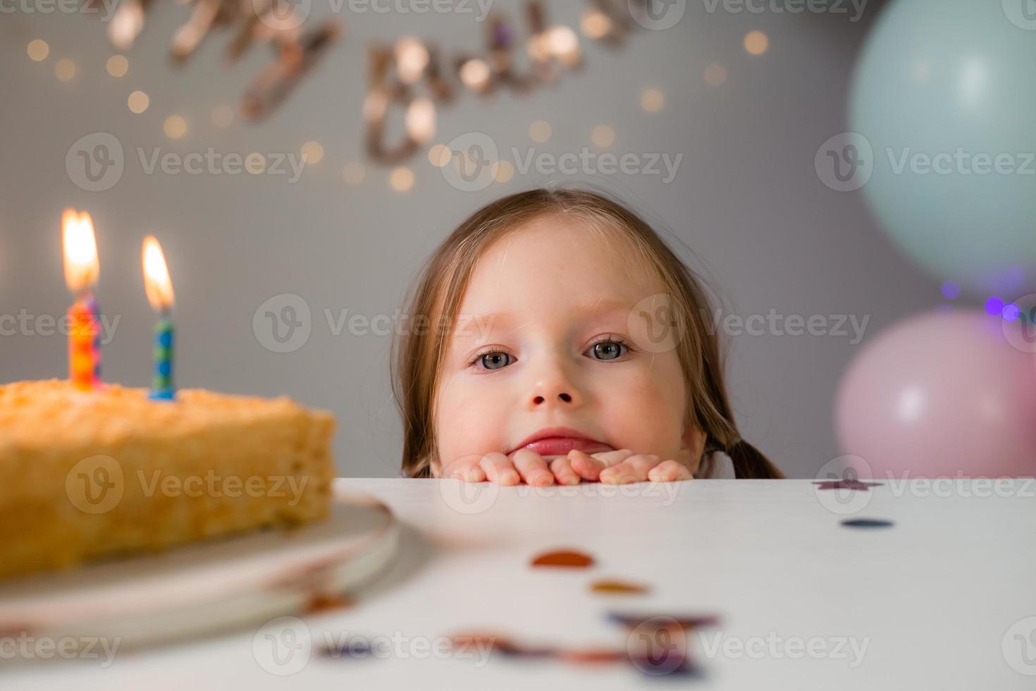 cute little girl blows out candles on a birthday cake at home against a backdrop of balloons. Child's birthday photo