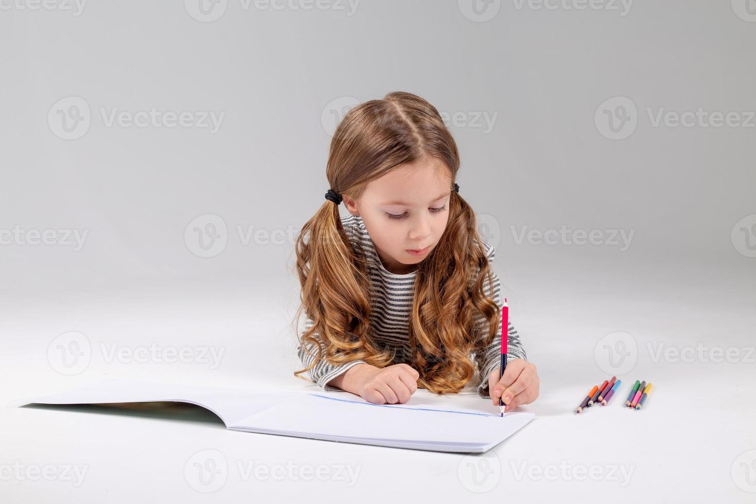 little girl in a striped dress draws in an album lying on the floor. child development. lifestyle. preschool and school education. space for text. High quality photo