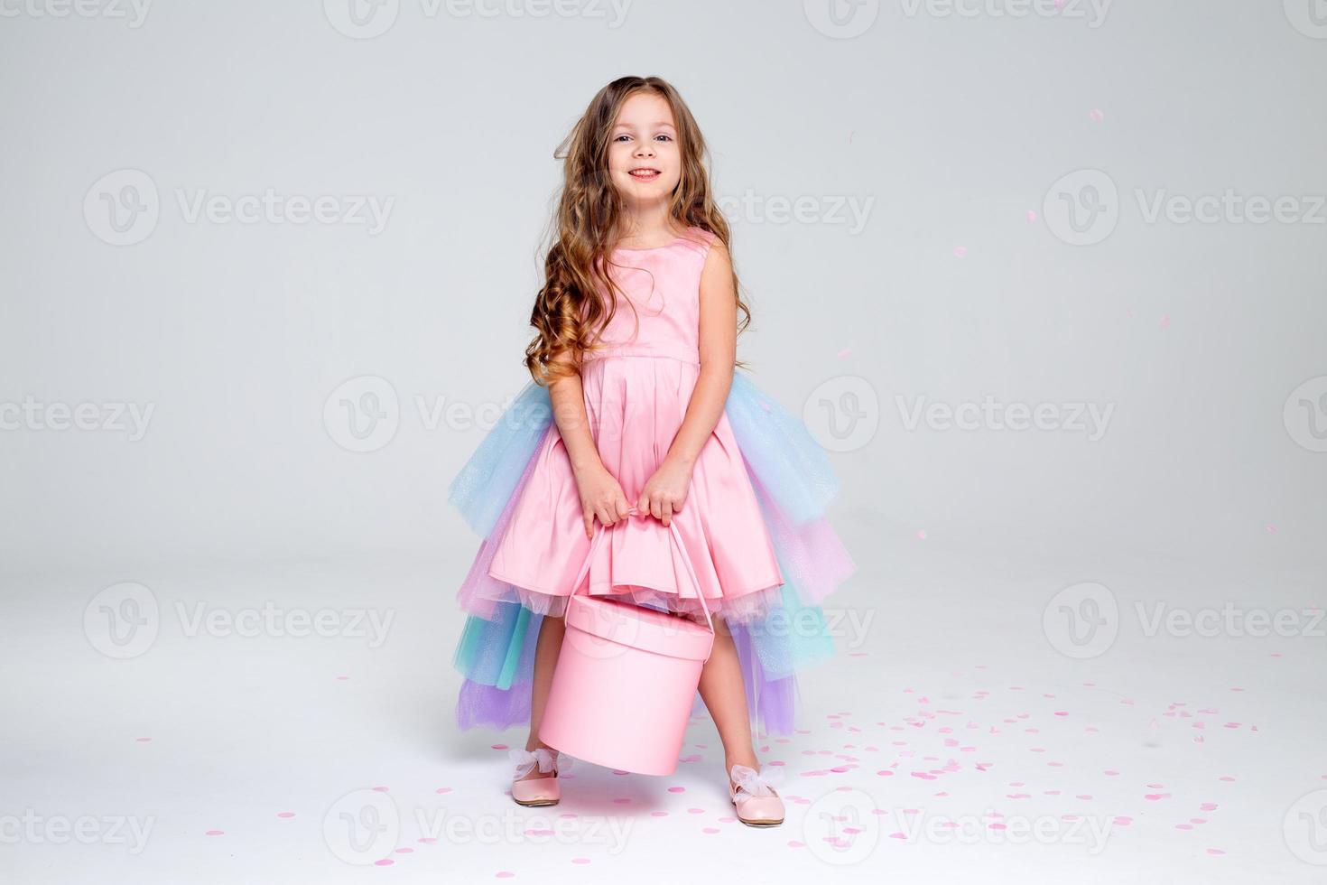 beautiful little girl in a chic pink dress poses sitting on a gray background and throws confetti. fashion and style. space for text. photo in the studio. High quality photo