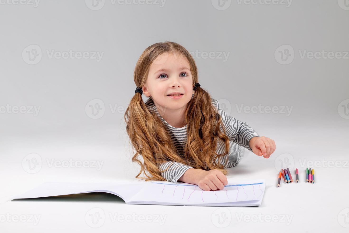 little girl in a striped dress draws in an album lying on the floor. child development. lifestyle. preschool and school education. space for text. High quality photo