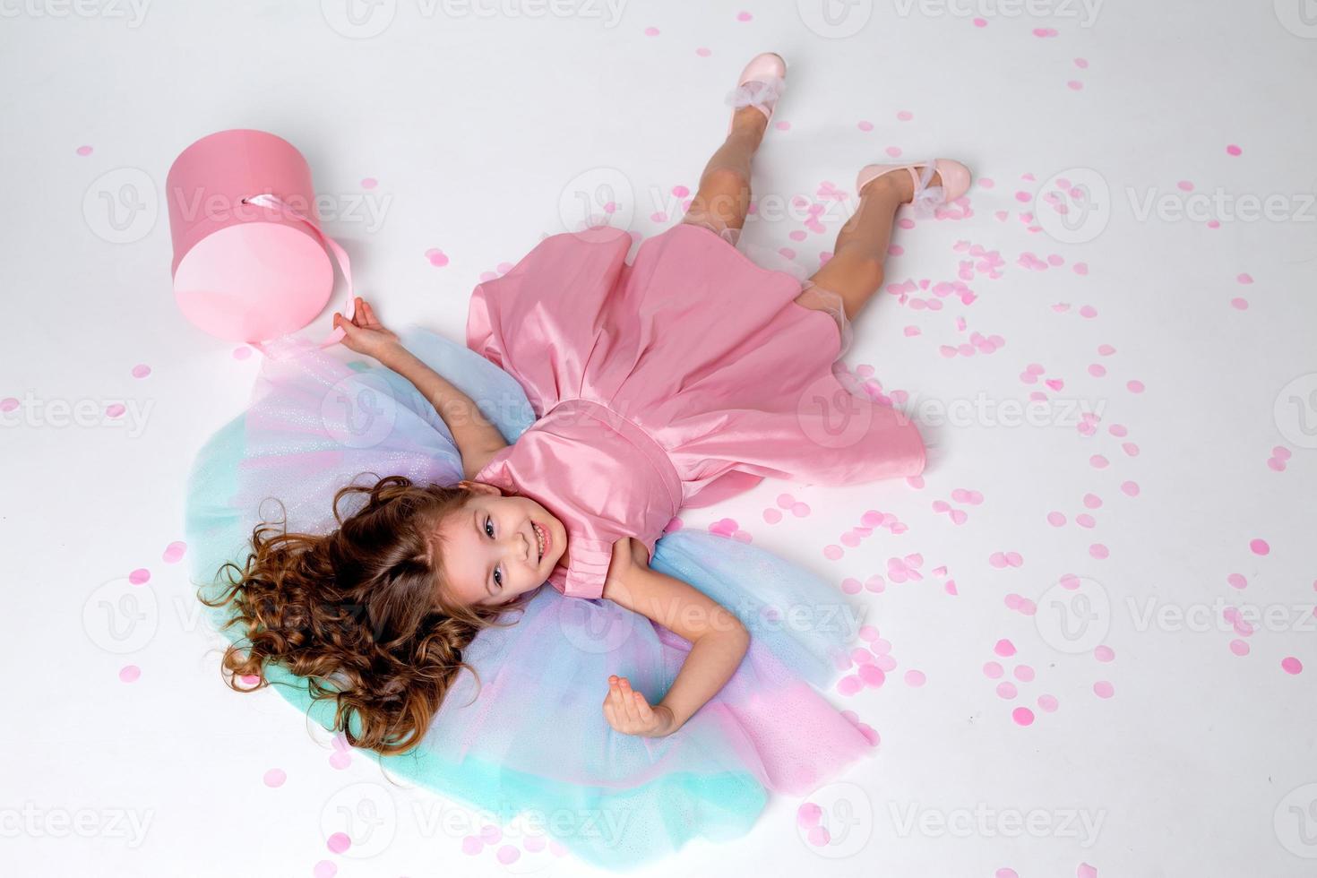 beautiful little girl in a chic pink dress poses sitting on a gray background and throws confetti. fashion and style. space for text. photo in the studio. High quality photo