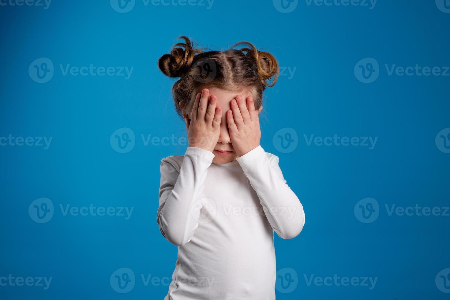 pequeño niña con un gracioso peinado en un blanco camiseta bebidas jugo desde un vaso. azul antecedentes. útil productos para niños. espacio para texto. alto calidad foto