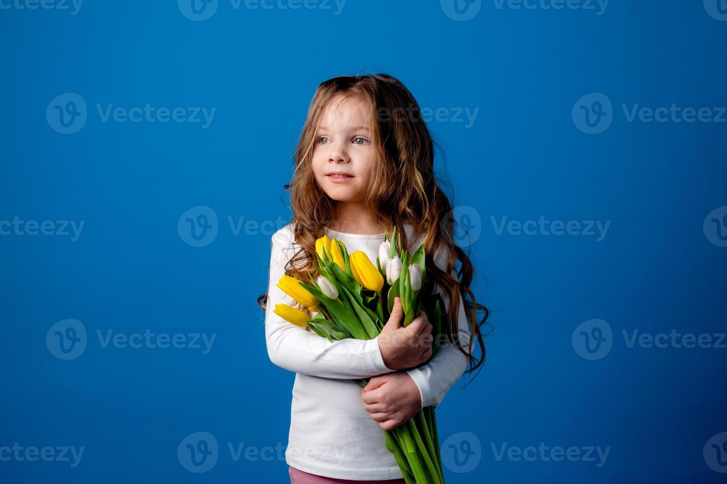 retrato de un encantador sonriente pequeño niña con un ramo de flores de tulipanes en su manos. estilo de vida. Fresco flores internacional De las mujeres día. espacio para texto. alto calidad foto