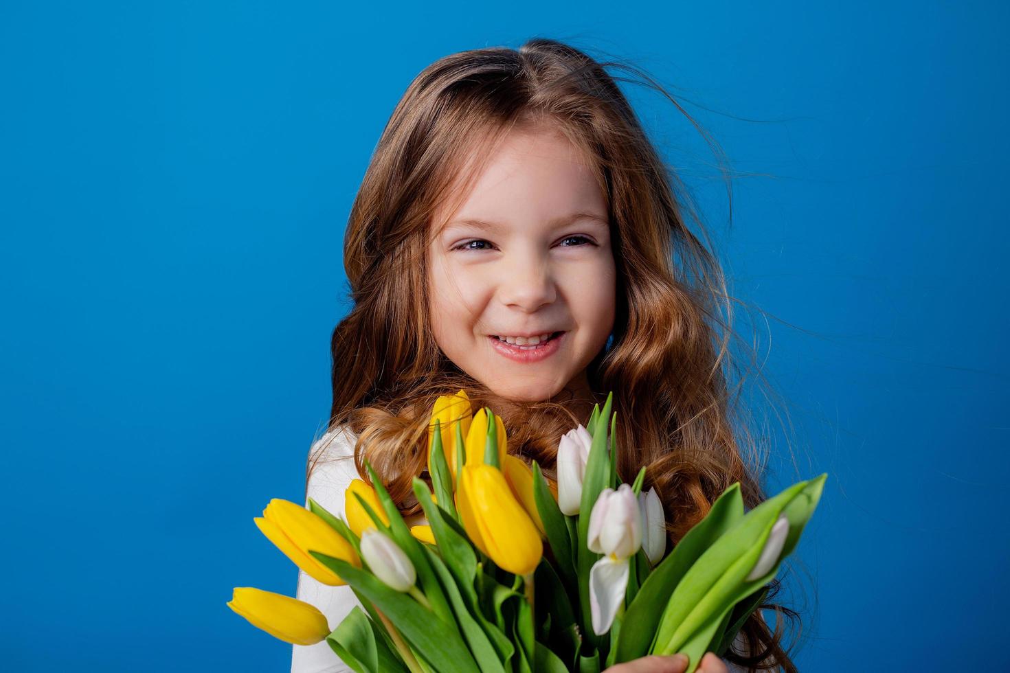 retrato de un encantador sonriente pequeño niña con un ramo de flores de tulipanes en su manos. estilo de vida. Fresco flores internacional De las mujeres día. espacio para texto. alto calidad foto