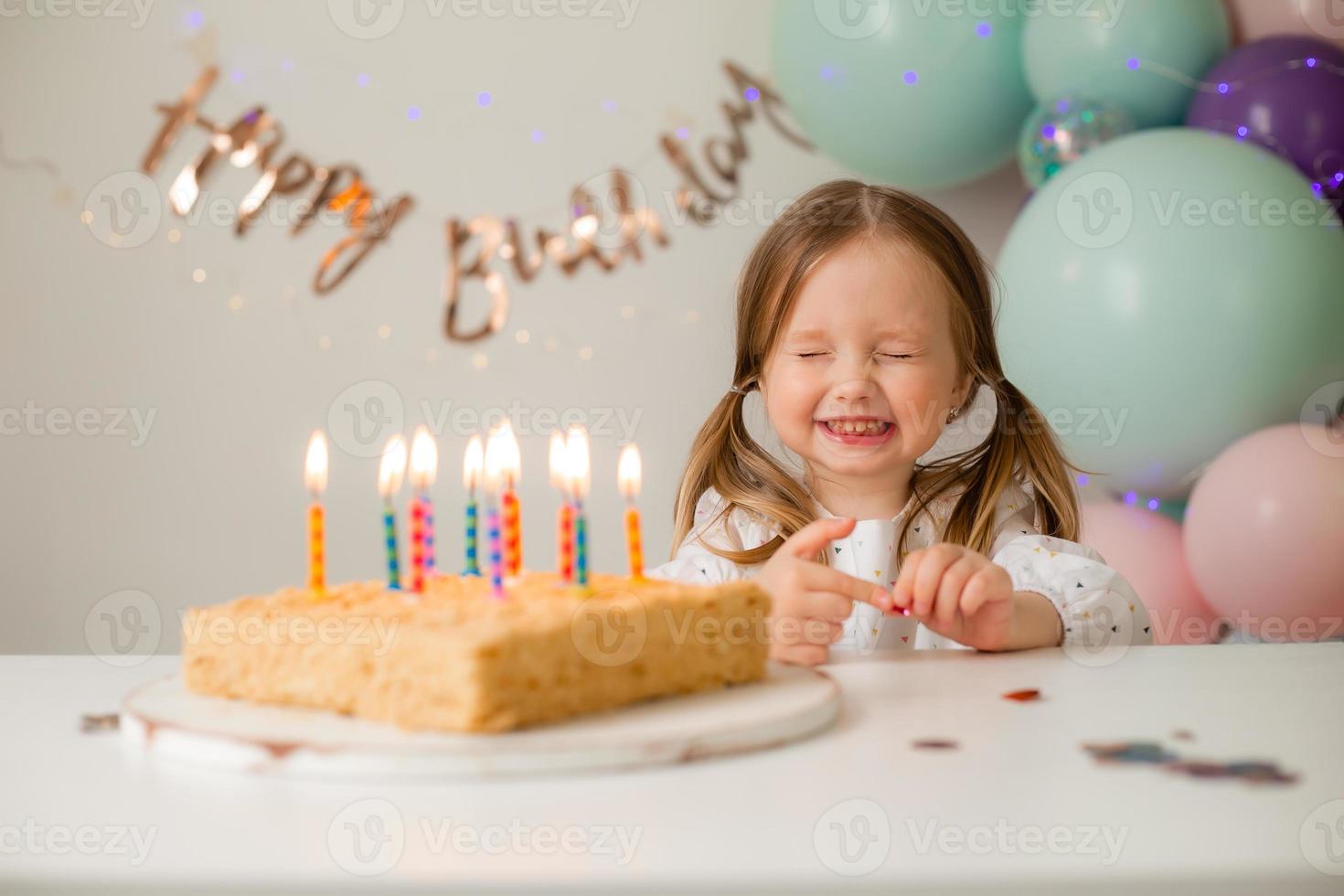 cute little girl blows out candles on a birthday cake at home against a backdrop of balloons. Child's birthday photo