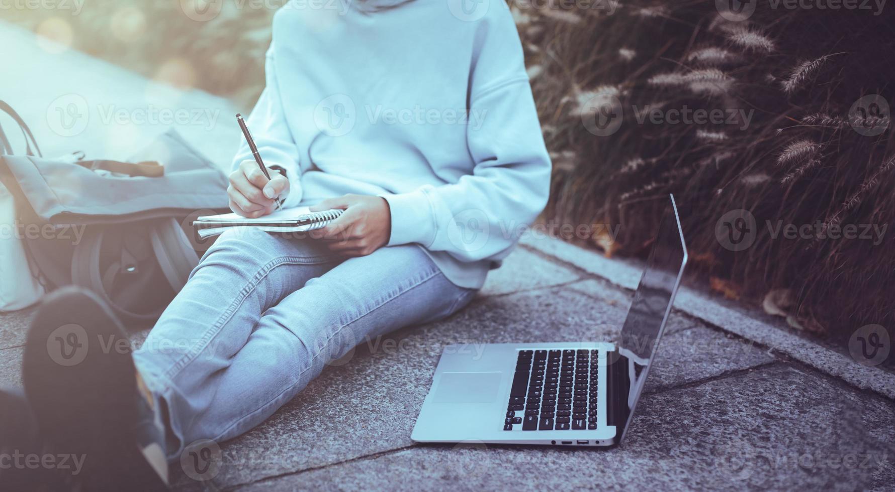 Man writing notebook with laptop in the park vintage style, Slim hipster man in jeans using a notebook, Freelancers, communication, Teenage student boy browses the Internet, working outside the home photo