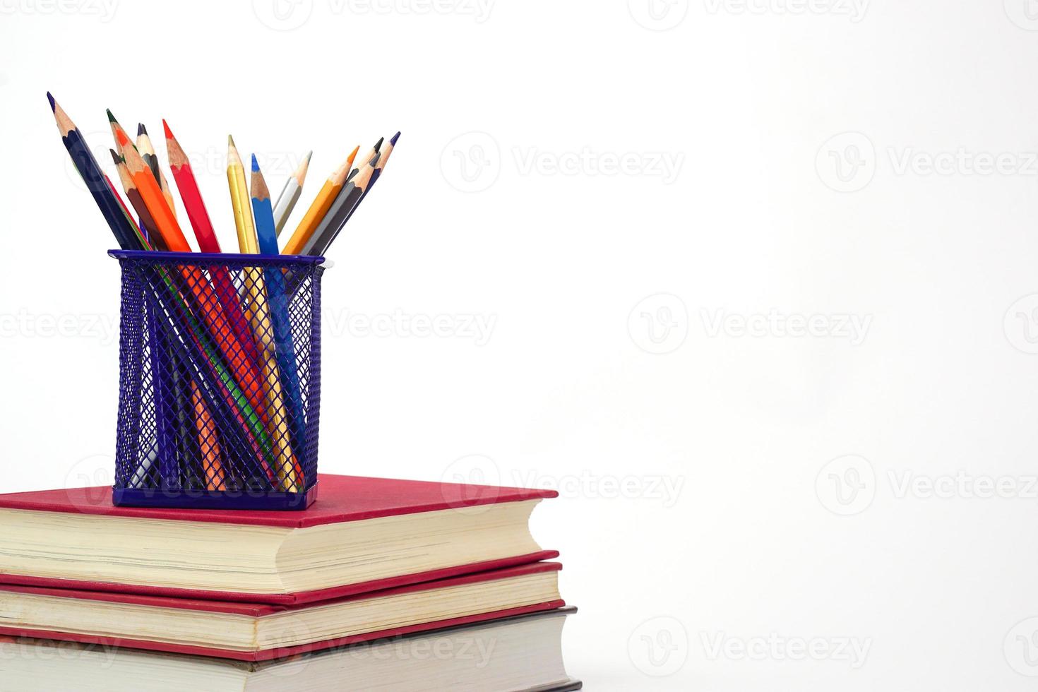 Crayon or colored pencils in box laying on a stack of books, white background. Knowledge and education concept. photo